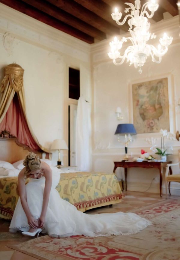 Wedding planner a Treviso Maria Mayer foto di sposa seduta su un letto in una stanza antica a Venezia mentre indossa una scarpa