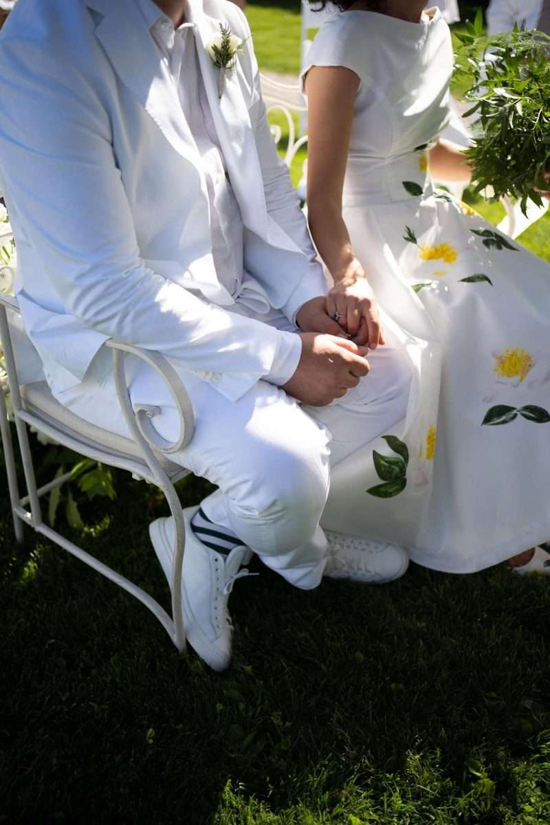 wedding planner Maria Mayer foto di Maria e Gian seduti su una panchina di metallo dipinta di bianco mentre stanno per fare le loro promesse durante il loro matrimonio primaverile ispirato al Royal Tea Party