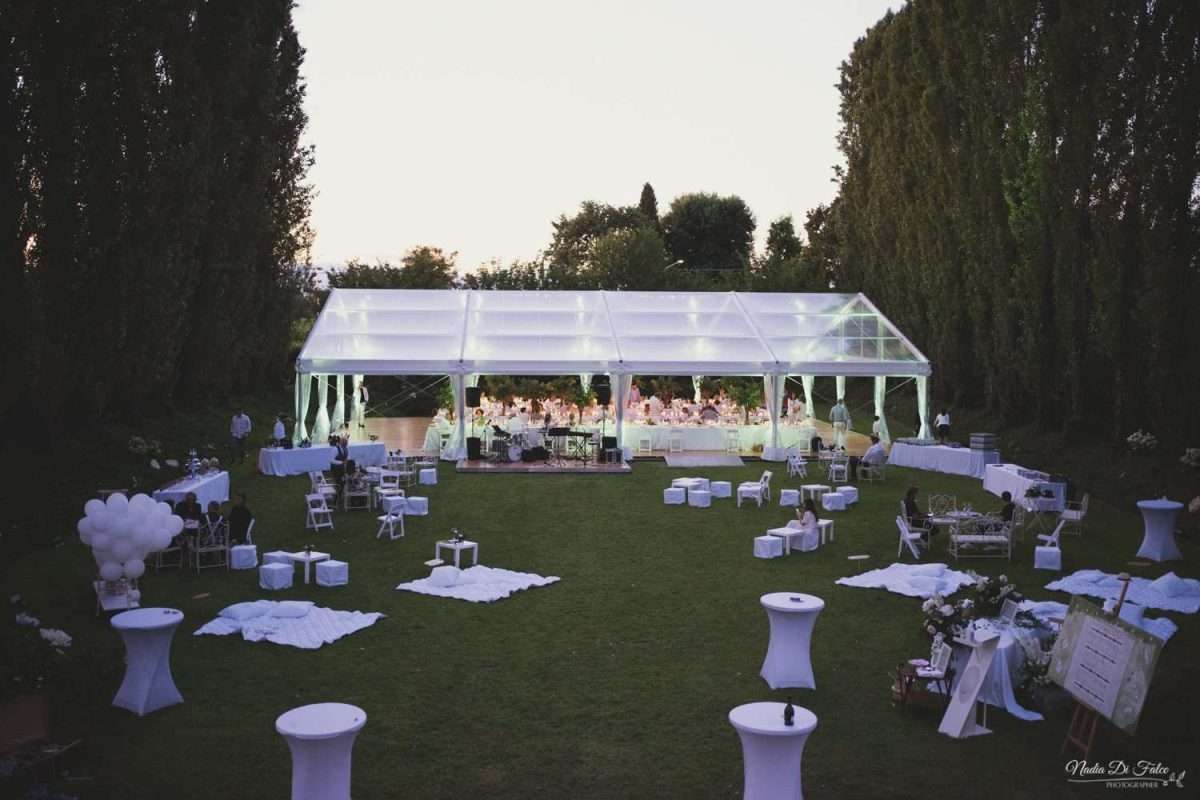 giardino di una location privata allestita per il matrimonio, nello sfondo struttura coperta che accoglie gli ospiti per la cena e nel resto del giardino pouf, sedie e coperte per poter rilassarsi