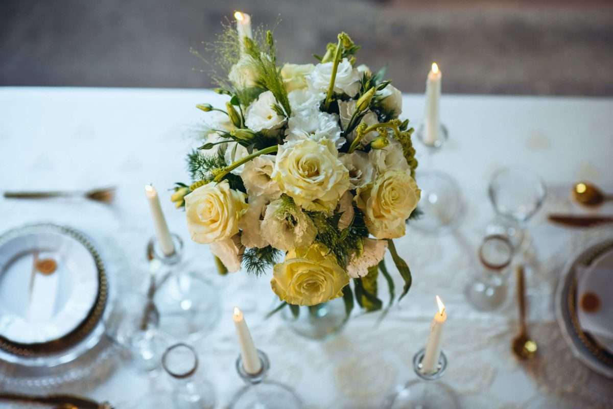 primo piano di un centro tavola per allestimento matrimonio composto da vari fiori bianchi, spiccano rose giallo tenue